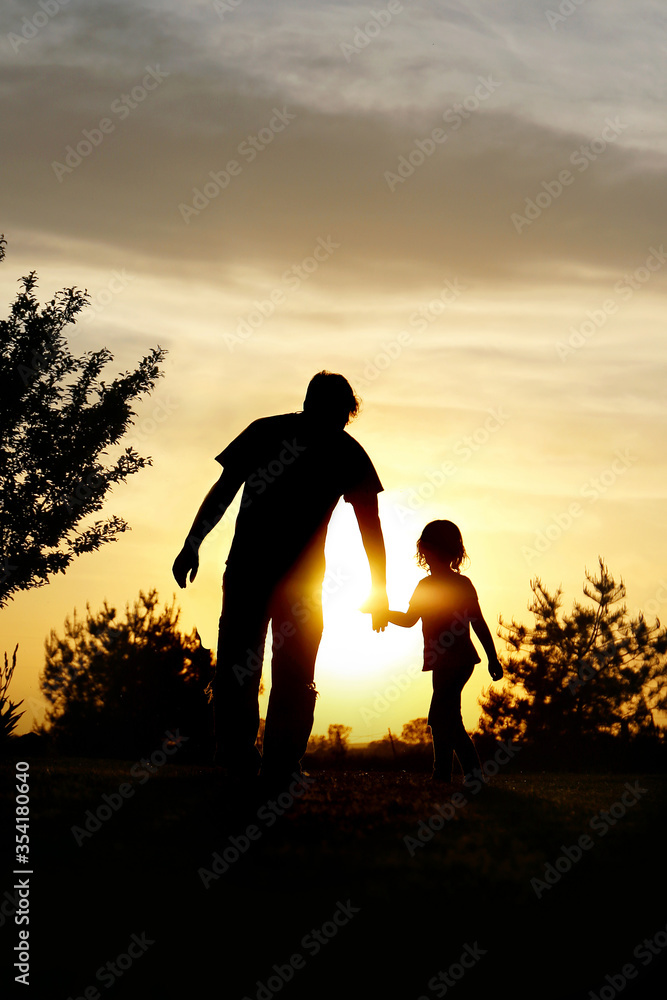 Happy Father and Young Child Walking Holding Hands at Sunset
