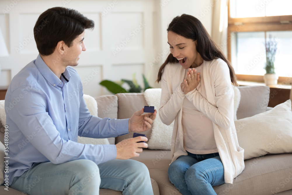 Loving caucasian young man present box with beautiful diamond wedding ring to overjoyed millennial beloved woman, affectionate male propose to excited female at home, engagement, marry me concept Loving caucasian young man present box with beautiful diamond wedding ring to overjoyed millennial beloved woman, affectionate male propose to excited female at home, engagement, marry me concept