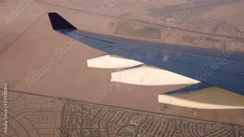 View from the left side window of an airplane on final approach to the Abu Dhabi International Airport making a left turn with trailing edge Flap system pods and a suburb in the background. photo