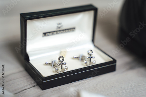 Close up of shiny anchor cufflinks in black padded box. Light background.