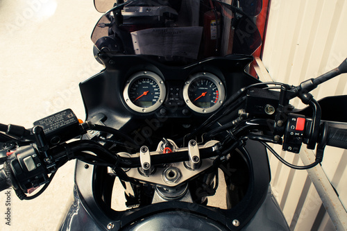 The arrow speedometer of a motorcycle on the steering wheel that stands on a concrete road closeup. Colored dashboard with sport bike handles  top view. Horizontal image of a tachometer gauge.