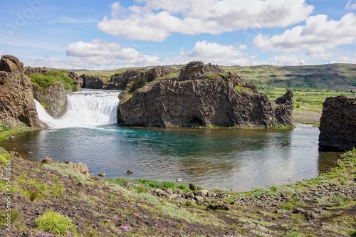 Hjalparfoss waterfall and basalt rocks in Iceland with azure water viewed from the top of a hill