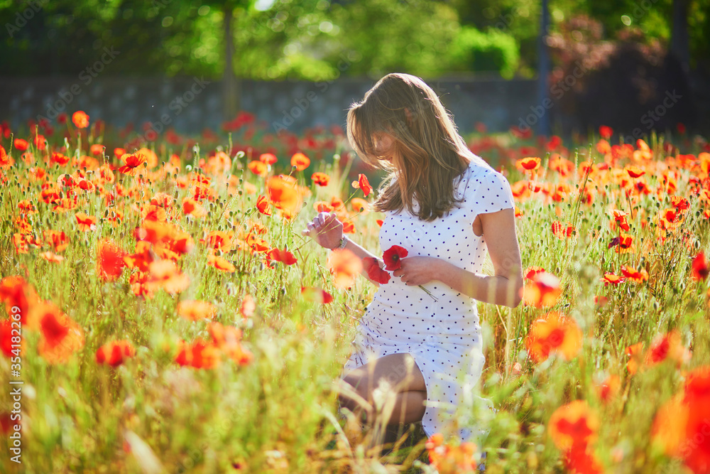 Beautiful young woman in white dress walking in poppy field on a summer day Beautiful young woman in white dress walking in poppy field on a summer day