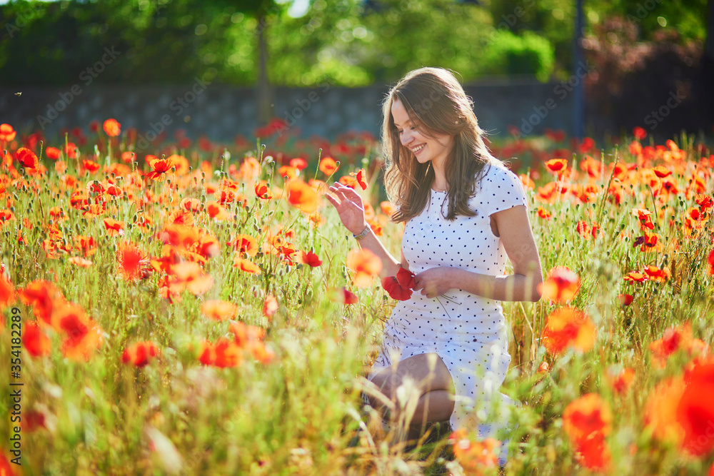 Beautiful young woman in white dress walking in poppy field on a summer day Beautiful young woman in white dress walking in poppy field on a summer day