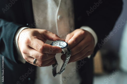Man in formal clothes holding luxury metal watches in hands. Businessman putting watches on wrist.