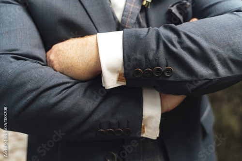 Elegant businessman in gray suit with hands on chest. Close up image of male hands. Jacket sleeve buttons and cufflinks detail.