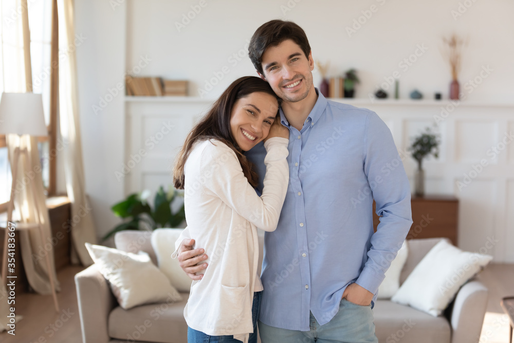 Portrait of happy young caucasian couple stand in new renovated home hug and cuddle excited to move in together, smiling man and woman posing in own house, relocating, realty, tenancy concept Portrait of happy young caucasian couple stand in new renovated home hug and cuddle excited to move in together, smiling man and woman posing in own house, relocating, realty, tenancy concept