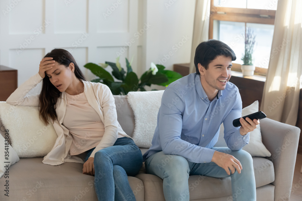Unhappy mad young woman sit separately angry at smiling man spouse watching football match on TV, millennial caucasian couple disagreement misunderstanding on television program or channel choice Unhappy mad young woman sit separately angry at smiling man spouse watching football match on TV, millennial caucasian couple disagreement misunderstanding on television program or channel choice