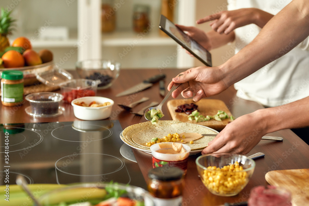 Close up of process of cooking. Man preparing meal while woman checking recipe using tablet. Vegetarians cooking in the kitchen together Close up of process of cooking. Man preparing meal while woman checking recipe using tablet. Vegetarians cooking in the kitchen together