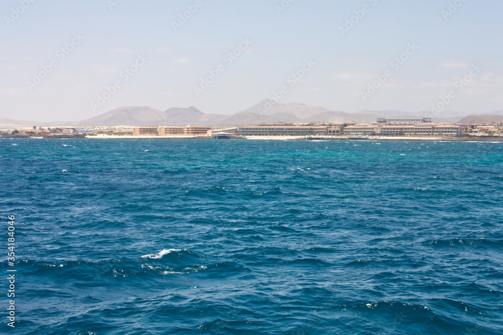 Seascape with choppy waves and blue sky looking toward Corralejo Fuertaventura from the sea with the Volcanos in the background. Space left for copy text.