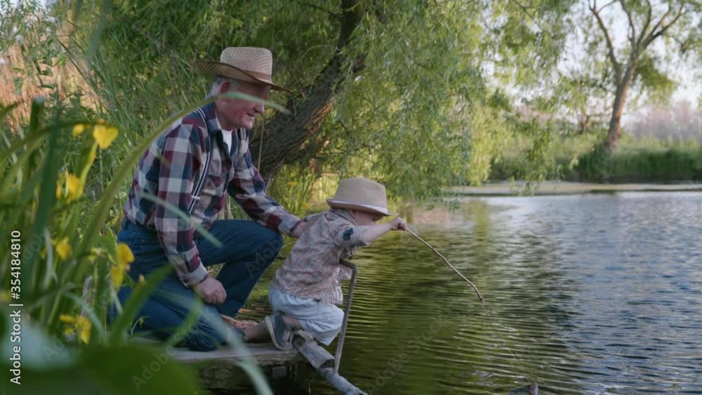 childhood, little cute male child together with his beloved grandfather, fisherman learns to fish in pond with fishing rod while relaxing by river in fine weather childhood, little cute male child together with his beloved grandfather, fisherman learns to fish in pond with fishing rod while relaxing by river in fine weather