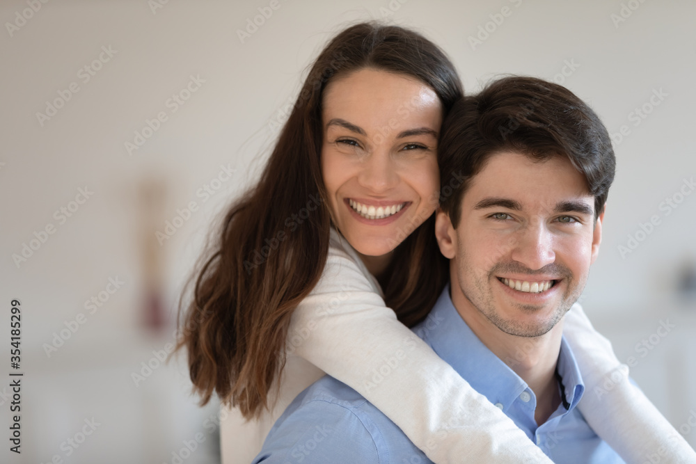 Close up portrait of happy young caucasian husband and wife hug look at camera posing for family picture together, smiling millennial couple have fun cuddle and embrace, show love and affection Close up portrait of happy young caucasian husband and wife hug look at camera posing for family picture together, smiling millennial couple have fun cuddle and embrace, show love and affection
