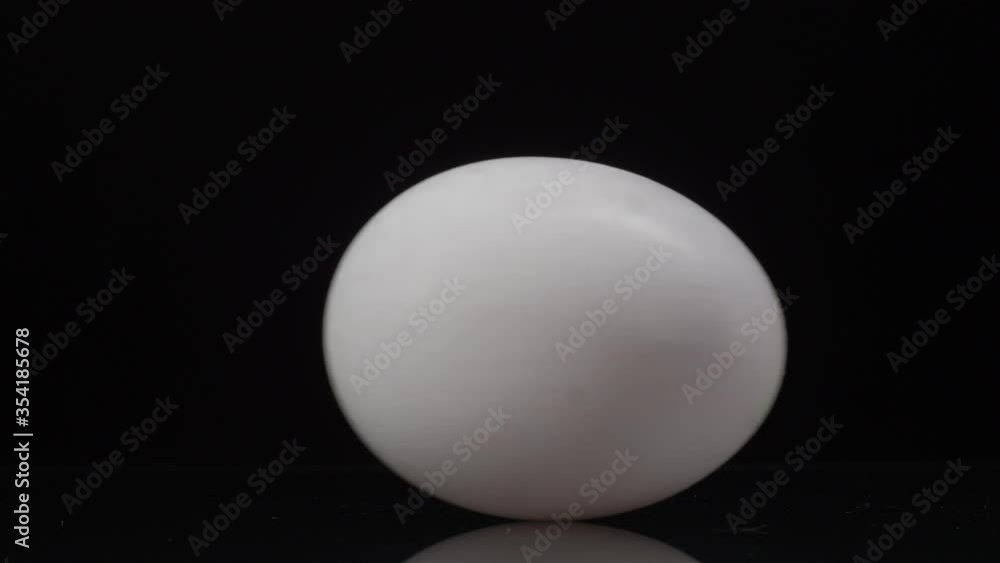 Egg rotation. White chicken egg spinning on a black background with reflection Egg rotation. White chicken egg spinning on a black background with reflection