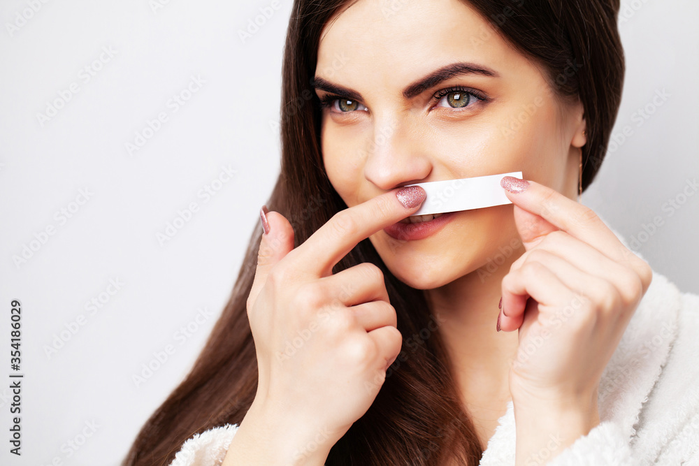 Young woman uses white stripe to remove hair in the face area Young woman uses white stripe to remove hair in the face area