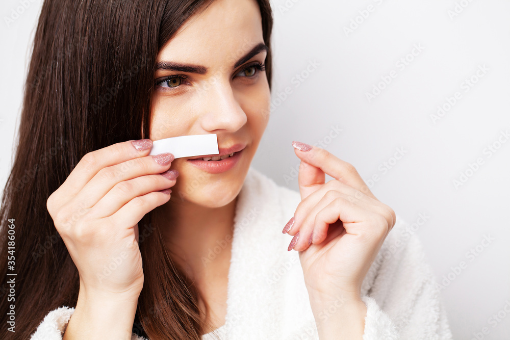 Young woman uses white stripe to remove hair in the face area Young woman uses white stripe to remove hair in the face area
