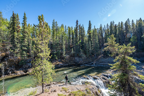 Fotografie Man standing beside a flowing creek with a small waterfall in northern British Columbia, Canada