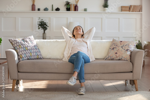 Happy calm young Caucasian woman relax on comfortable modern sofa in living room nap or sleep, relaxed girl rest on couch at home, relive negative emotion, breathe fresh air, stress free concept