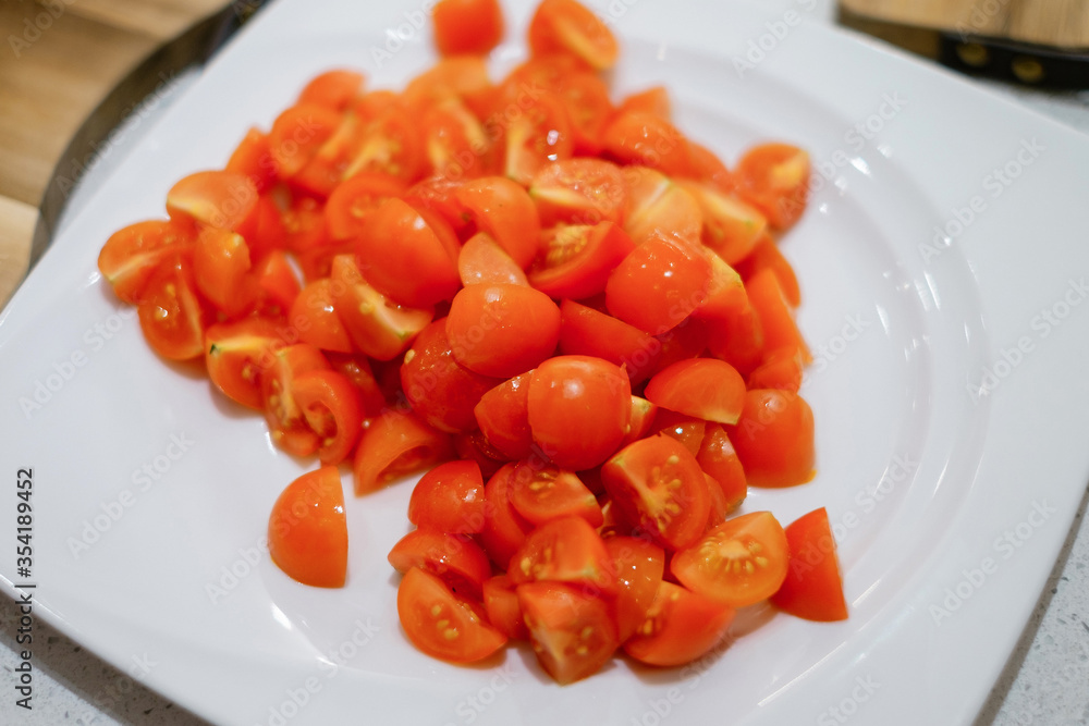 Chopped tomato on a white plate. People making salad together awaiting guests. Concept of home cooking healthy food.