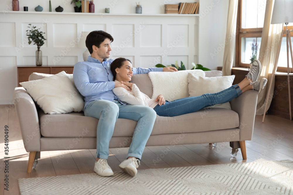 Happy millennial man and woman relax on comfortable couch in living room hugging and cuddling together, smiling dreamy young couple rest on sofa at home, embrace look in distance visualizing Happy millennial man and woman relax on comfortable couch in living room hugging and cuddling together, smiling dreamy young couple rest on sofa at home, embrace look in distance visualizing