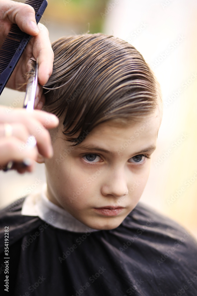 Fototapeta premium Barber cuts the boy with scissors