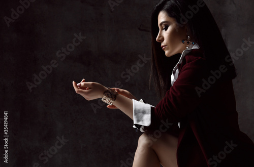 Portrait of young stylish woman brunette in black jacket and white shirt fastening he bracelet on her hand on grey photo