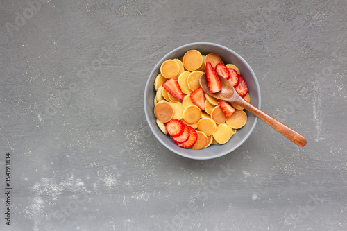 Breakfast of mini pancakes with sliced strawberries on a gray background. photo