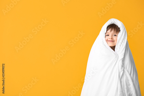 Little boy wrapped in blanket on color background © Pixel-Shot