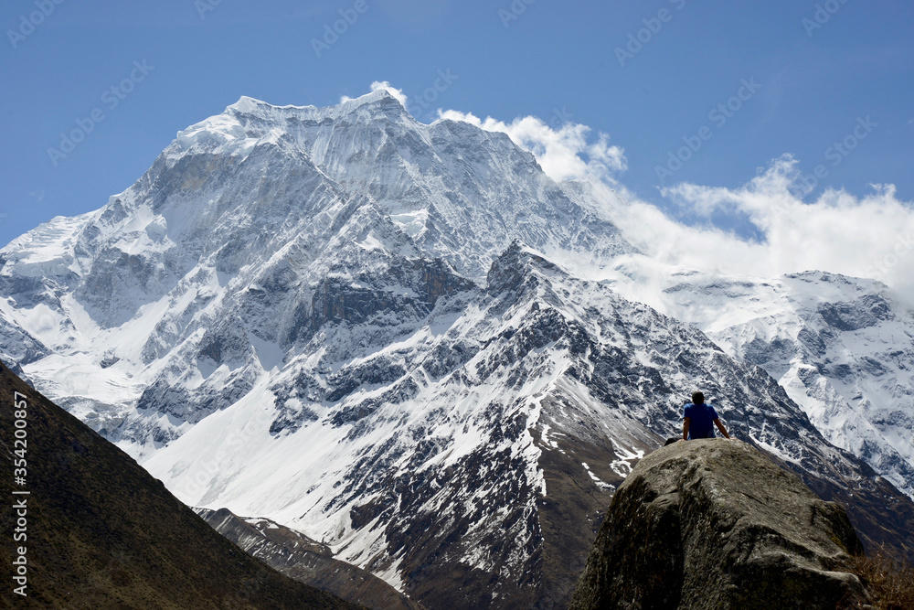 Man sitting on a rock contemplating the Himalaya mountains in front of him during a trek along the Manaslu Circuit in Nepal