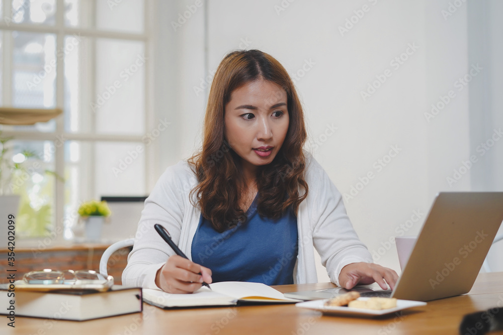 Asian people study online course via internet. Young girl watching business lesson from laptop computer and note lecture to notebook at home. Asian people study online course via internet. Young girl watching business lesson from laptop computer and note lecture to notebook at home.