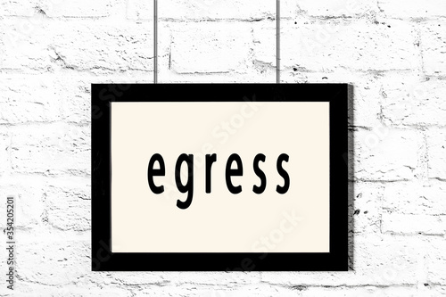 Black frame hanging on white brick wall with inscription egress