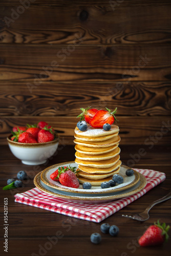 A big stack of homemade classic american pancakes with fresh blueberries and strawberries on wooden background.