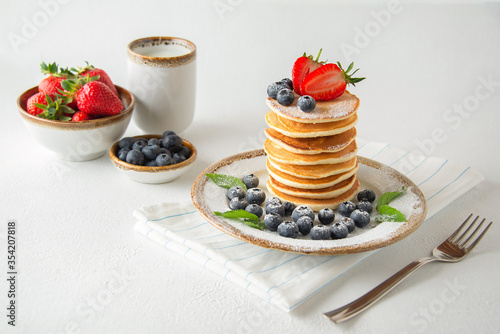 Stack of pancakes with fresh blueberries, strawberries, powdered sugar and cup of milk. Healthy breakfast.