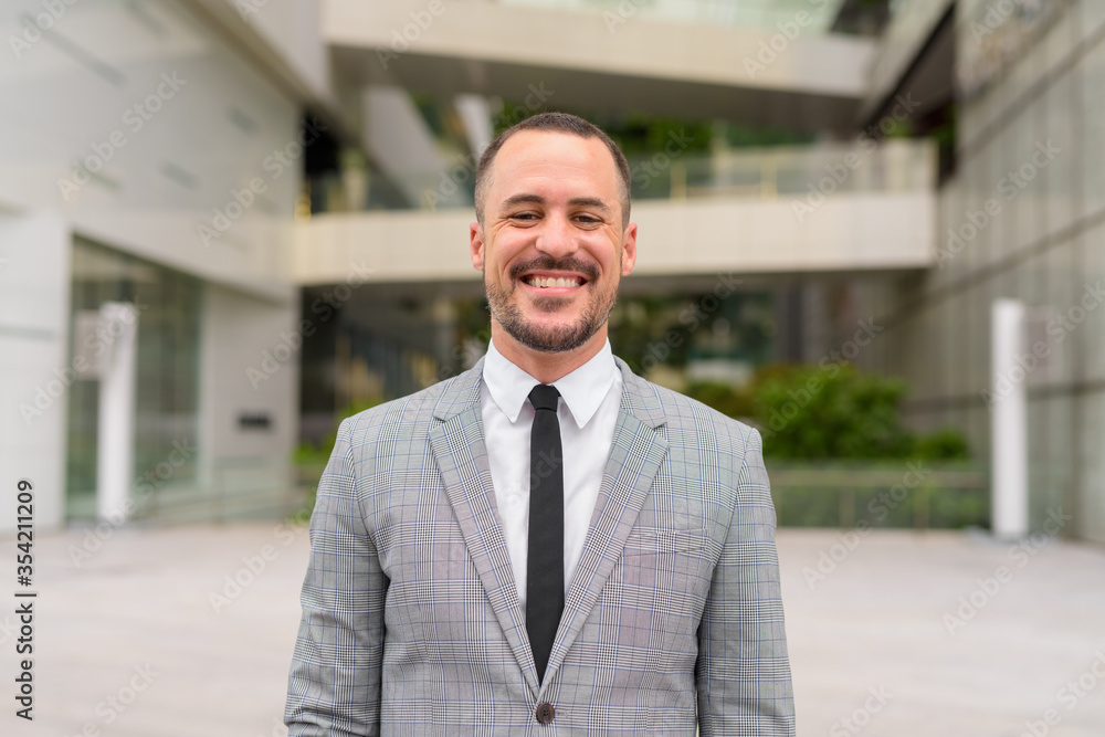 Happy Hispanic bald bearded businessman smiling in the city outdoors Happy Hispanic bald bearded businessman smiling in the city outdoors