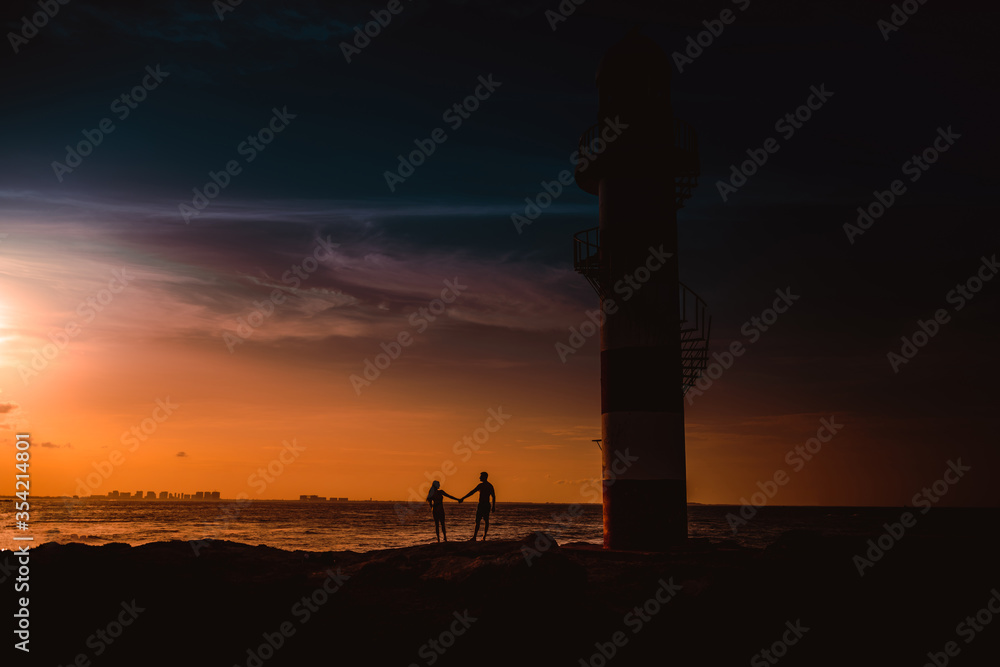 Fototapeta premium The silhouette of a couple and a huge lighthouse.