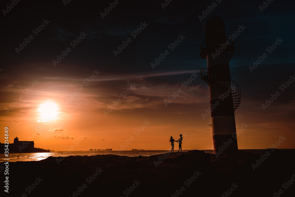 The silhouette of a couple and a huge lighthouse.