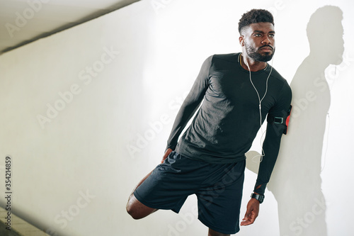 Serious handsome young Black sportsman stretching legs after jogging in the morning