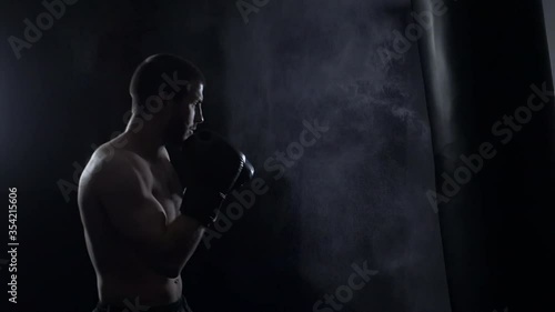 Fighter Practicing Some Kicks With Punching Bag. Kick, punching bag on dark background. Black punching bag weighs at the gym