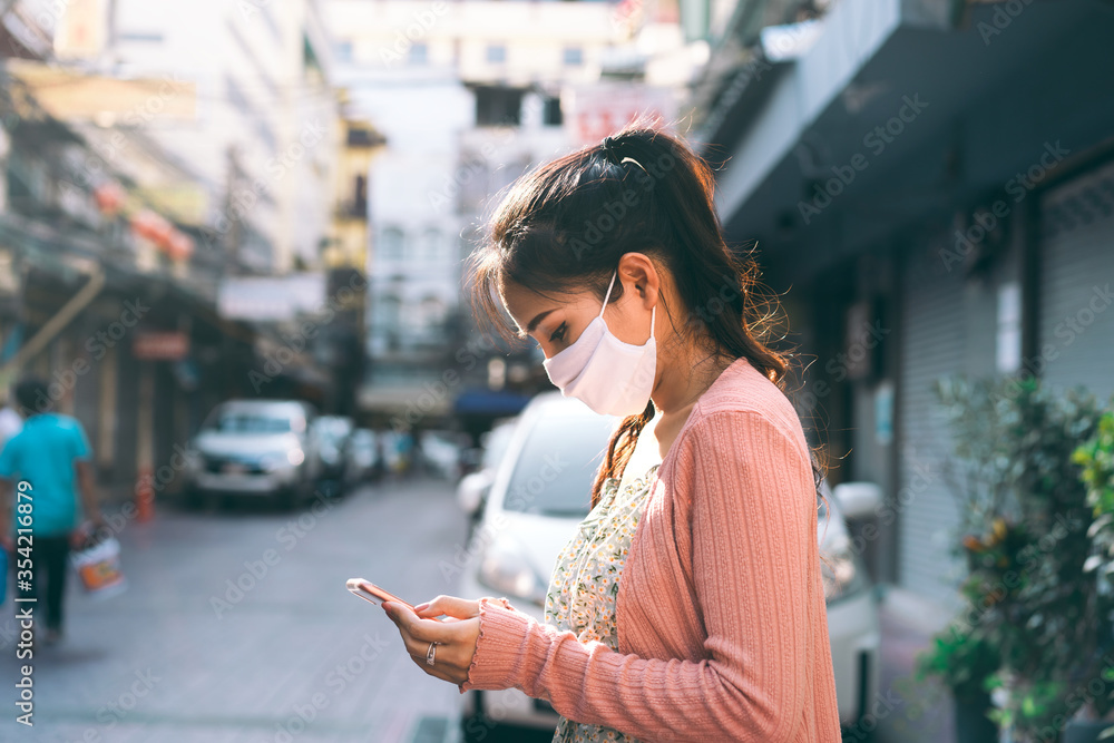 Fototapeta premium Asian adult woman tan skin wear mask on face and using smartphone.
