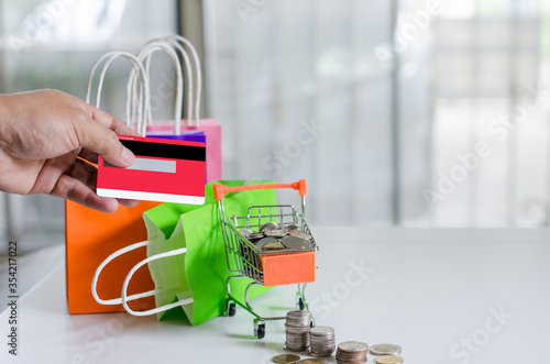 Hand holding  credit card and small cart with paper bag and coin have on it online shopping located in home concept of detention at home to prevent the Covid19 virus.