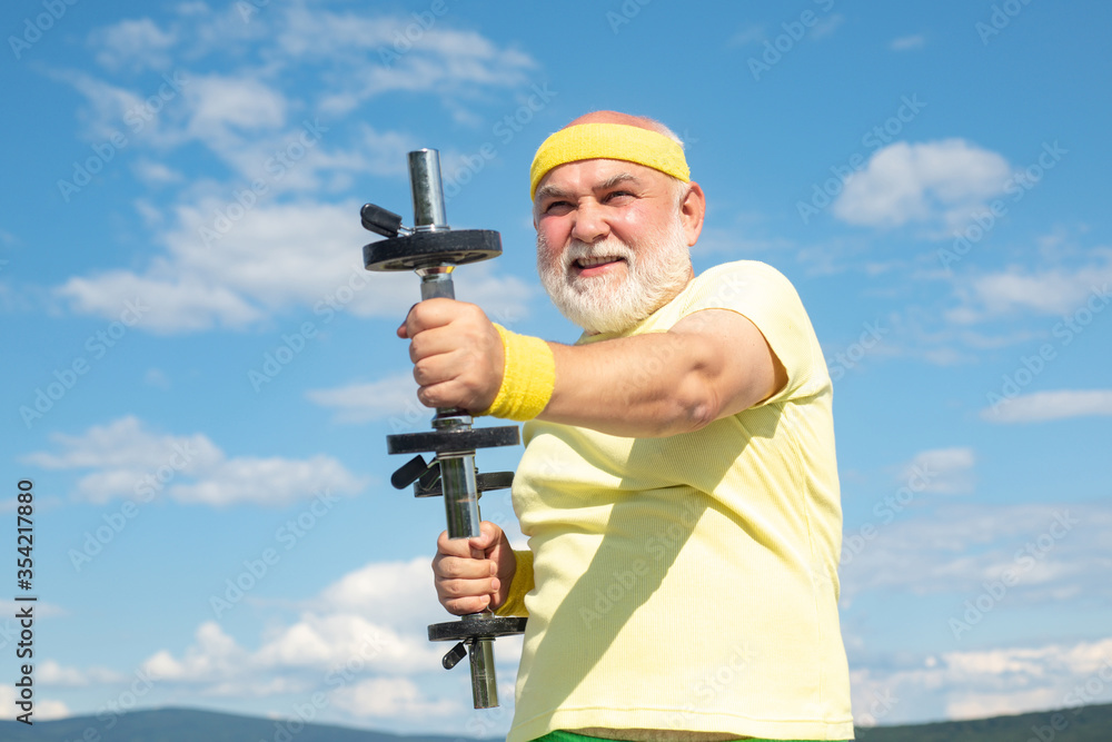 Senior fitness man training with dumbbells isolated on blue background. Age is no excuse to slack on your health. Be in motion. Senior fitness man training with dumbbells isolated on blue background. Age is no excuse to slack on your health. Be in motion.