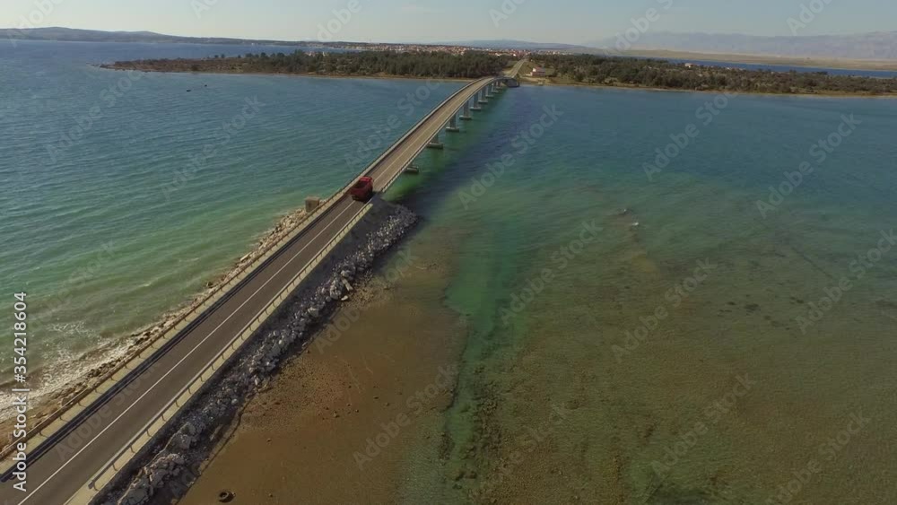 Aerial shot of truck on bridge over sea against blue sky, drone flying forward over ocean on sunny day - Razanac, Croatia Aerial shot of truck on bridge over sea against blue sky, drone flying forward over ocean on sunny day - Razanac, Croatia