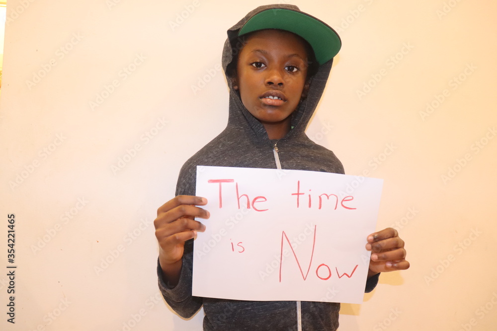 Black Child holding paper with words The time is now written in red indoors white background Black Child holding paper with words The time is now written in red indoors white background