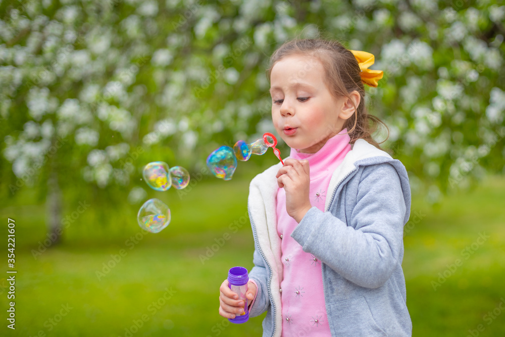 Beautiful little blonde girl, has happy fun cheerful smiling face, soap bubble blower.
