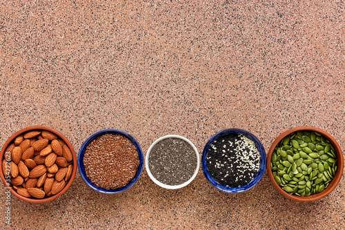 Different seeds in a bowl in a row on a brown stone background. Sesame, flax, chia, pumpkin, almonds. Top view, flat lay, copy space.