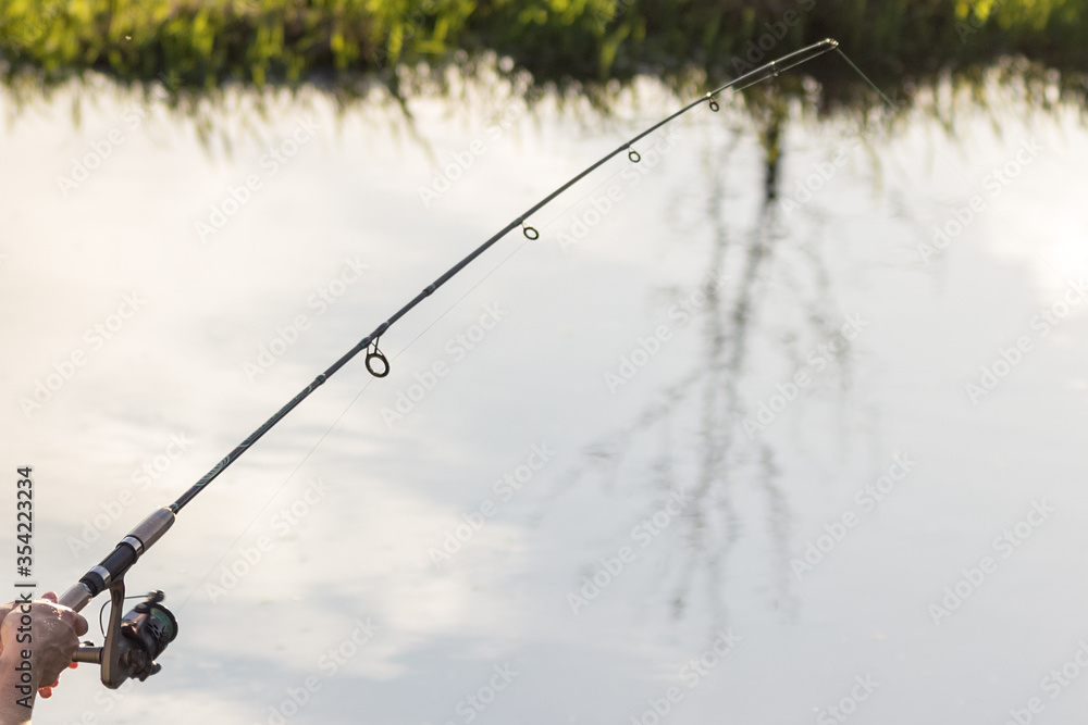 Fishing rod in the hands of a fisherman on the lake. beautiful hands with spinning on the background of water. concept for fisherman's day and summer fishing. hobby Fishing rod in the hands of a fisherman on the lake. beautiful hands with spinning on the background of water. concept for fisherman's day and summer fishing. hobby