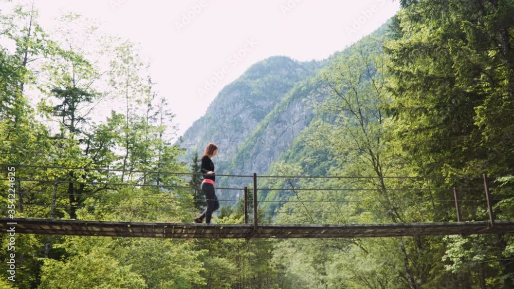 Caucasian woman walks on hanging wooden bridge, Beautiful mountain river Soča under, forest in background, sunny day, 4K. Caucasian woman walks on hanging wooden bridge, Beautiful mountain river Soča under, forest in background, sunny day, 4K.