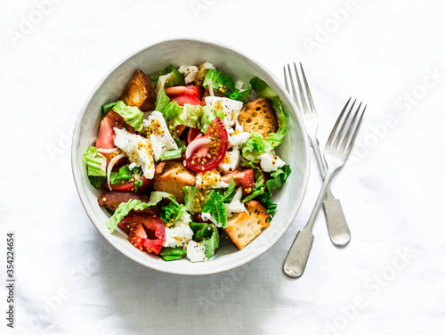 Rustic italian salad with fresh tomatoes  crispy ciabatta  mozzarella cheese  green salad with olive oil  mustard  lemon dressing on a light background  top view