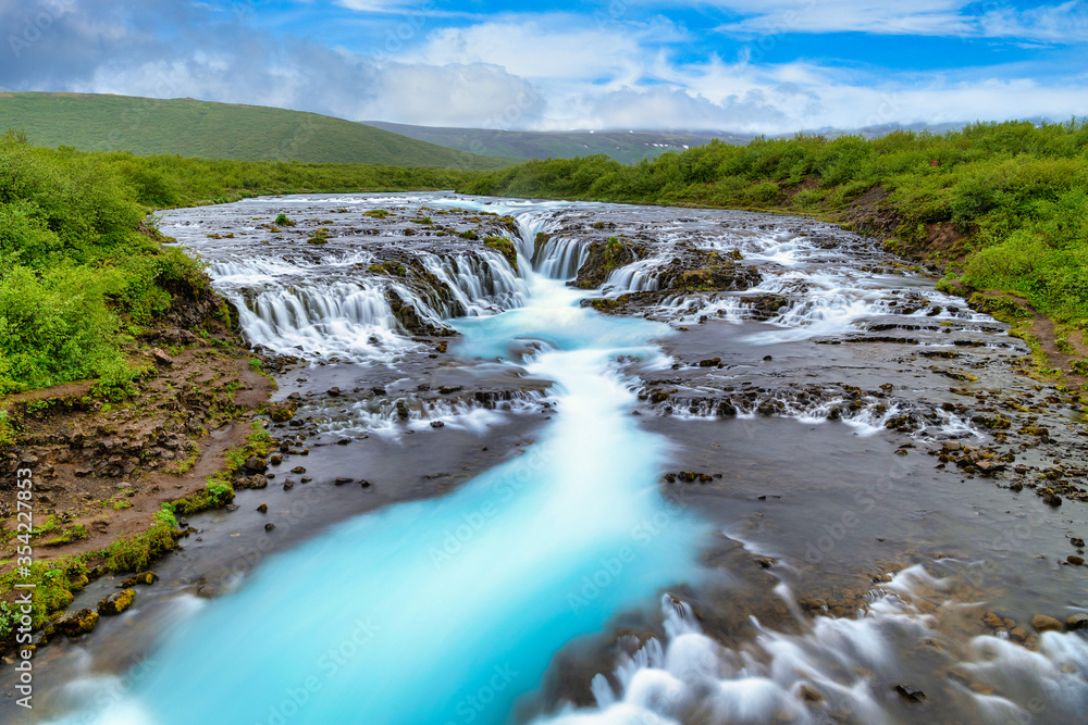 Bruarfoss Waterfall in the summer, with trees and green grass all over the area. This is a waterfall that is hidden among nature in Iceland. Bruarfoss Waterfall in the summer, with trees and green grass all over the area. This is a waterfall that is hidden among nature in Iceland.