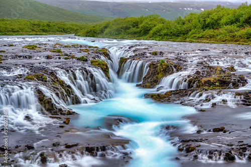 Bruarfoss Waterfall in the summer  with trees and green grass all over the area. This is a waterfall that is hidden among nature in Iceland.