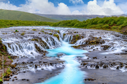 Bruarfoss Waterfall in the summer  with trees and green grass all over the area. This is a waterfall that is hidden among nature in Iceland.